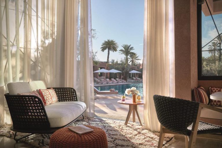 Habitación con terraza y vista a la piscina exterior rodeada de palmeras en Royal Mansour Marrakech