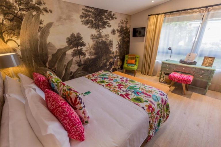 Habitación doble con mural tropical y ropa de cama floral colorida en el hotel Patio del Mundo