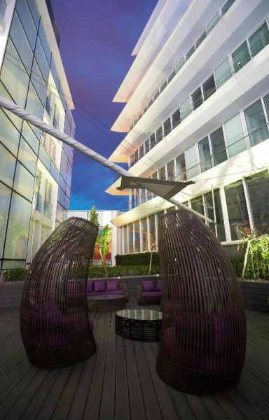 Terraza lounge exterior con cabinas de mimbre y cojines morados en The Vine Hotel