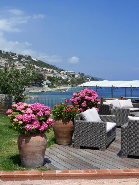 Terraza exterior del Hotel Alivi con sofás de ratán, macetas de hortensias rosas y vistas al mar