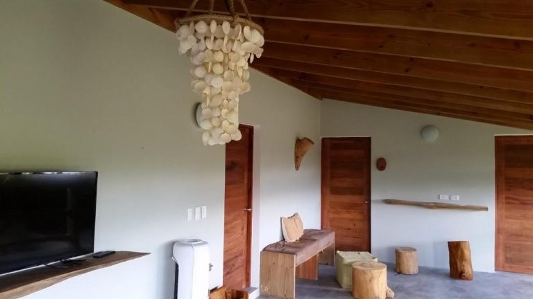 Salón rústico con lámpara de conchas, mobiliario de madera natural y TV en Residencia El Balatà