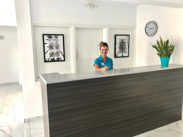 Recepcionista sonriente en el mostrador de recepción de Margarita Napa Apartments en Ayia Napa