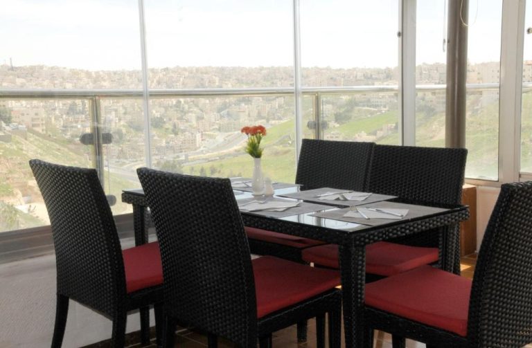 Restaurante con mesas y sillas negras del Olive Hotel Amman con vistas panorámicas a la ciudad