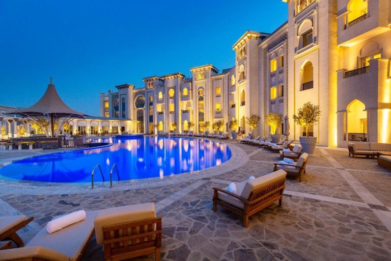 Piscina exterior iluminada del Ezdan Palace Hotel con tumbonas y arquitectura árabe de lujo al atardecer