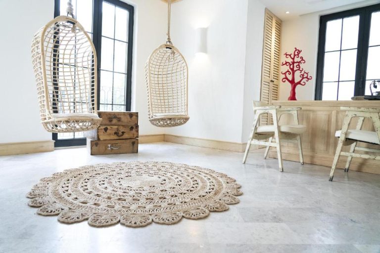 Salón bohemio con sillas colgantes de ratán y alfombra redonda en Yacht Boheme Hotel-Boutique