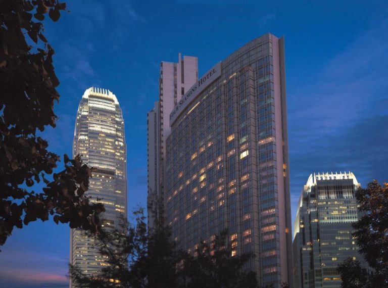 Fachada exterior nocturna del Four Seasons Hotel Hong Kong con rascacielos iluminados al atardecer