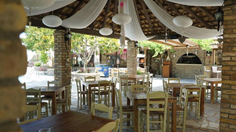 Terraza restaurante al aire libre con mesas de madera y techo de madera en Spiti Nikos