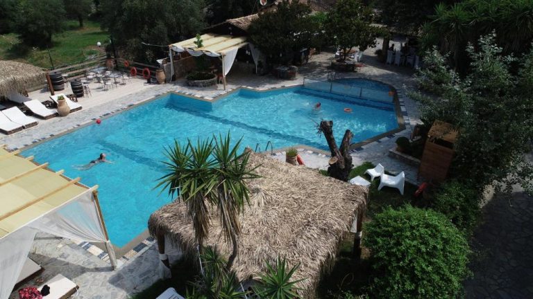 Piscina exterior con zona tropical y bar de paja en Spiti Nikos, rodeada de vegetación mediterránea