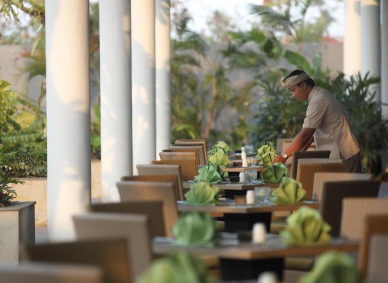 Terraza del restaurante del Hotel Santika Siligita Nusa Dua con mesas decoradas y jardín tropical