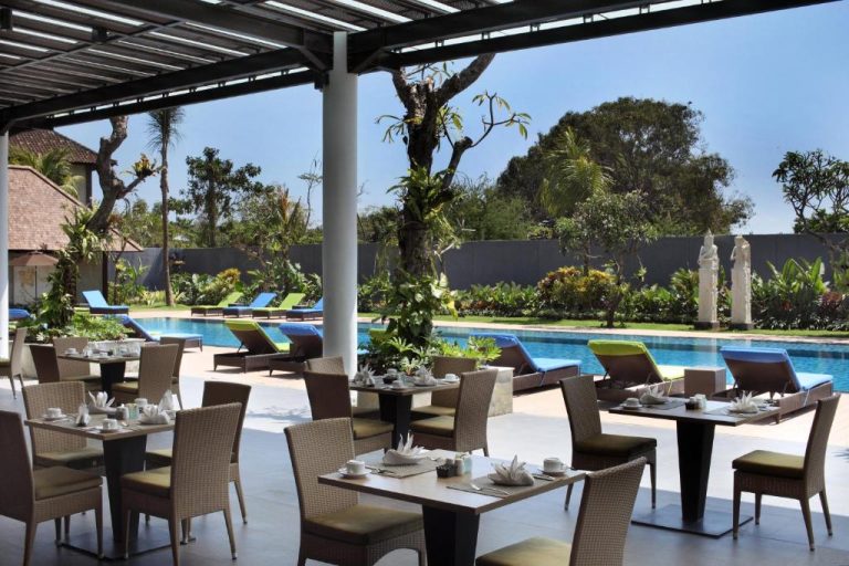 Restaurante al aire libre con mesas junto a la piscina del Hotel Santika Siligita Nusa Dua en Bali