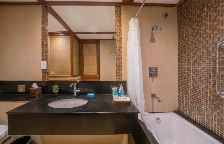 Baño con bañera, ducha y lavabo de mármol negro en The Blue Water Geoffrey Bawa Heritage Resort