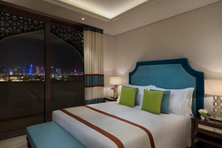 Habitación de lujo con cama doble y vistas nocturnas al skyline de Doha en Al Najada Doha Hotel Apartments by Oaks