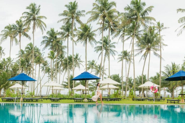 Piscina infinita con sombrillas y palmeras tropicales en The Blue Water Geoffrey Bawa Heritage Resort
