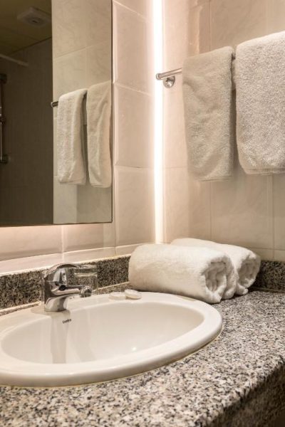 Baño moderno con lavabo de porcelana y toallas blancas en el Hotel Mayfair Gardens