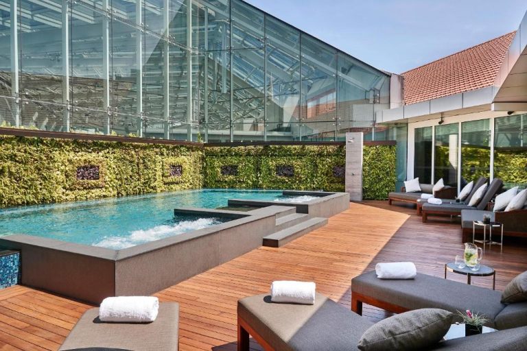 Piscina exterior con jacuzzi y terraza de madera del Capitol Kempinski Hotel Singapore rodeada de jardín vertical