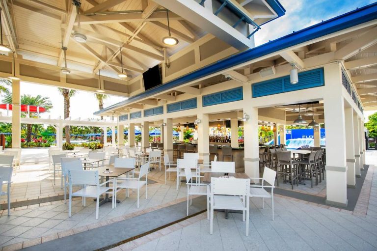 Restaurante bar al aire libre con mesas blancas junto al parque acuático en The Grove Resort Orlando