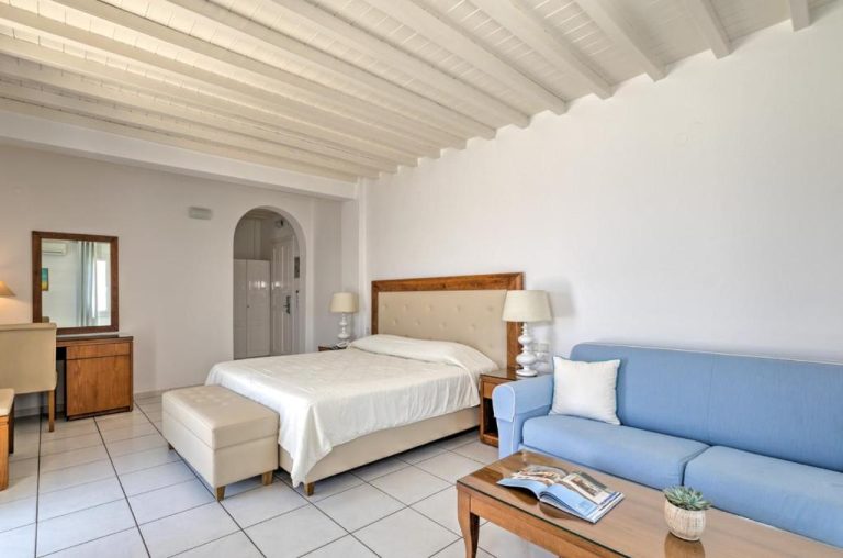 Habitación doble con cama y sofá azul en Hotel Alkyon, decoración mediterránea blanca y techo de vigas