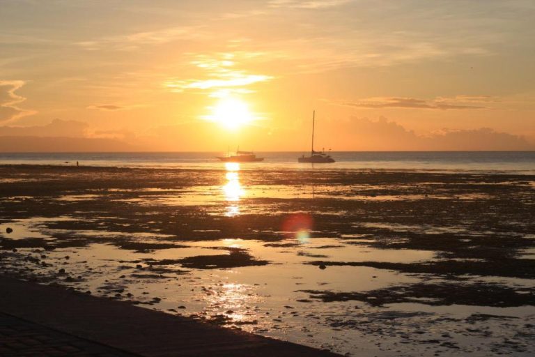Impresionante puesta de sol sobre la playa de The Beachhouse Cebu con veleros en el horizonte