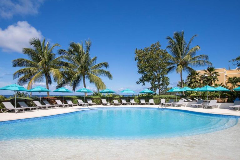 Piscina exterior con tumbonas y sombrillas turquesas rodeada de palmeras en Beach View Hotel