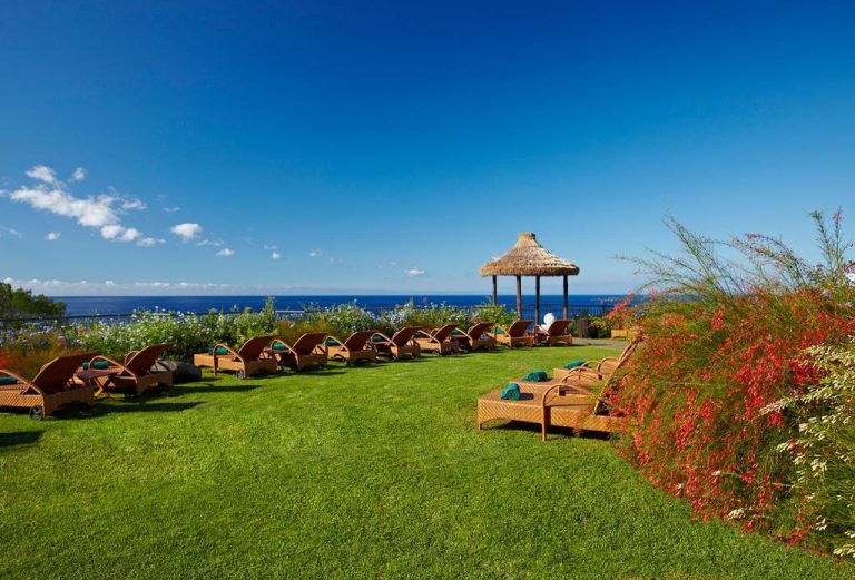 Jardines con hamacas de madera y gazebo de paja con vistas al mar en Hotel Porto Mare PortoBay