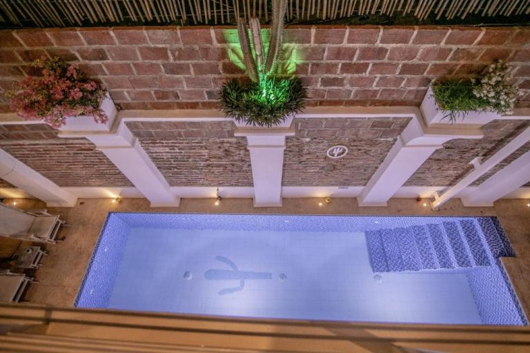 Piscina interior iluminada con patio colonial de ladrillo en El Cactus Luxury Apartments del centro histórico