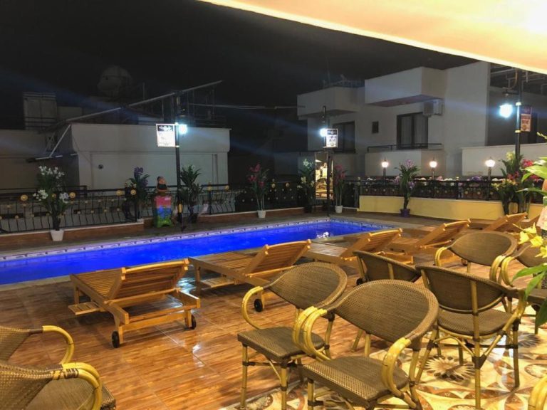 Piscina exterior iluminada de noche con tumbonas y sillas en el Hotel Marko Pasa Konagi