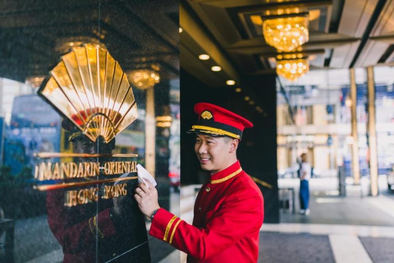 Portero uniformado limpiando la fachada de mármol en la entrada del Mandarin Oriental Hong Kong