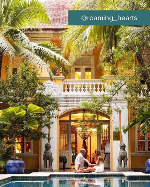 Pareja junto a la piscina exterior rodeada de jardín tropical en The Pavilion Hotel