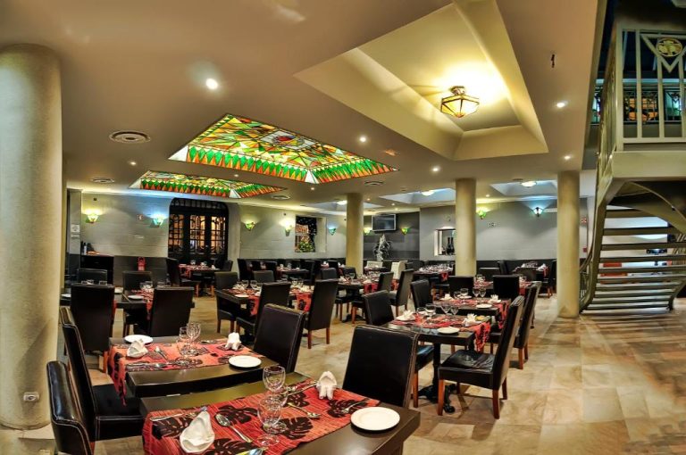 Elegante restaurante del Hotel Talisman con mesas decoradas, vitrales en el techo y escalera interior