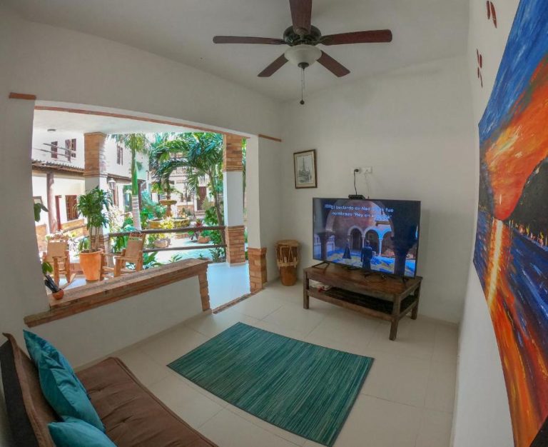 Sala de estar con televisor y vista al patio tropical con fuente en Camali Hotel