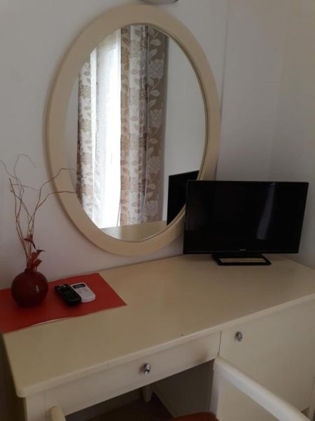 Escritorio blanco con espejo ovalado y televisión en habitación del Pulades Resort