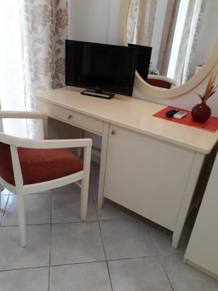 Escritorio blanco con televisión y espejo en habitación del Pulades Resort con silla tapizada en rojo