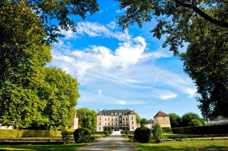 Fachada principal y jardines exteriores del Château de Saulon rodeado de árboles y cielo azul