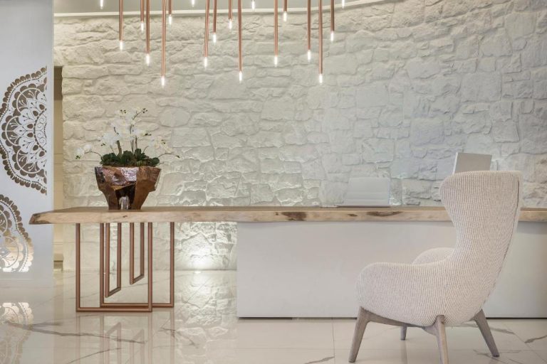 Recepción de lujo del Palladium Hotel con pared de piedra blanca, mesa de madera y lámpara de cobre