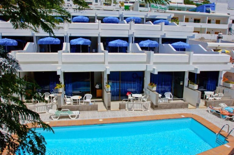 Piscina exterior y terrazas con sombrillas azules de los Apartamentos Monte Verde en Lanzarote