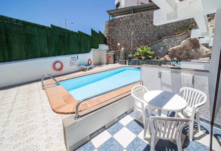 Piscina exterior con terraza y sillas blancas en Apartamentos Monte Verde, zona de baño con salvavidas