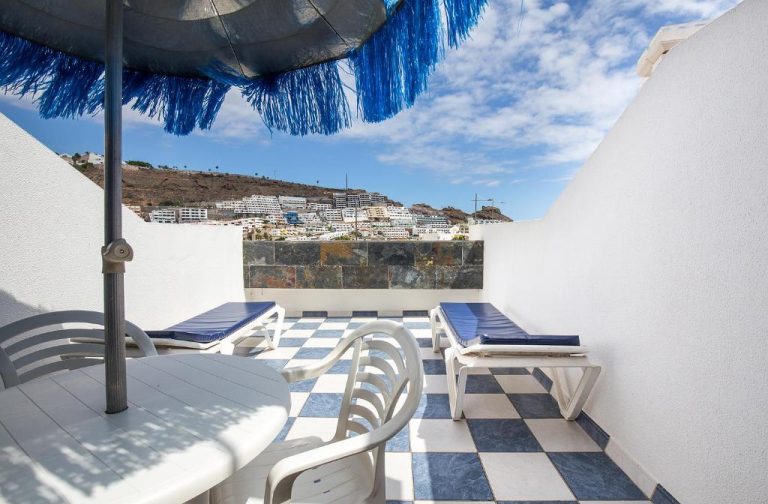 Terraza con tumbonas y sombrilla azul en Apartamentos Monte Verde con vistas a Puerto Rico Gran Canaria