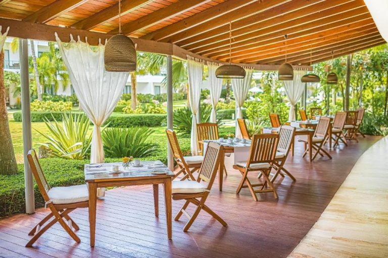Terraza restaurante exterior con mesas de madera y jardines tropicales en el hotel Sublime Samaná