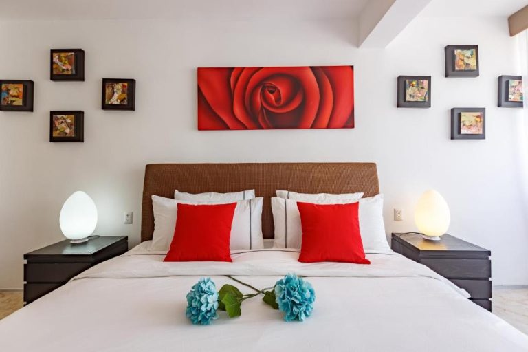 Habitación doble con cama king, cojines rojos y cuadro de rosa roja en Magia Beachside Condo