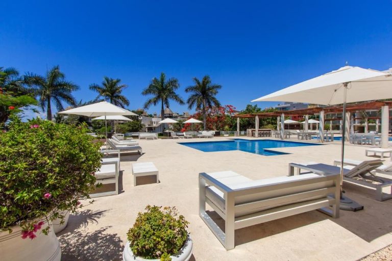 Piscina exterior con tumbonas y sombrillas blancas en Magia Beachside Condo rodeada de palmeras
