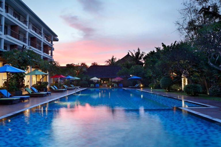 Piscina exterior al atardecer con tumbonas y sombrillas del Hotel Santika Siligita Nusa Dua en Bali