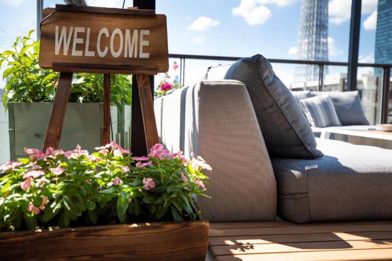 Terraza exterior con sofá lounge, plantas y cartel de bienvenida en el Sola Hotel
