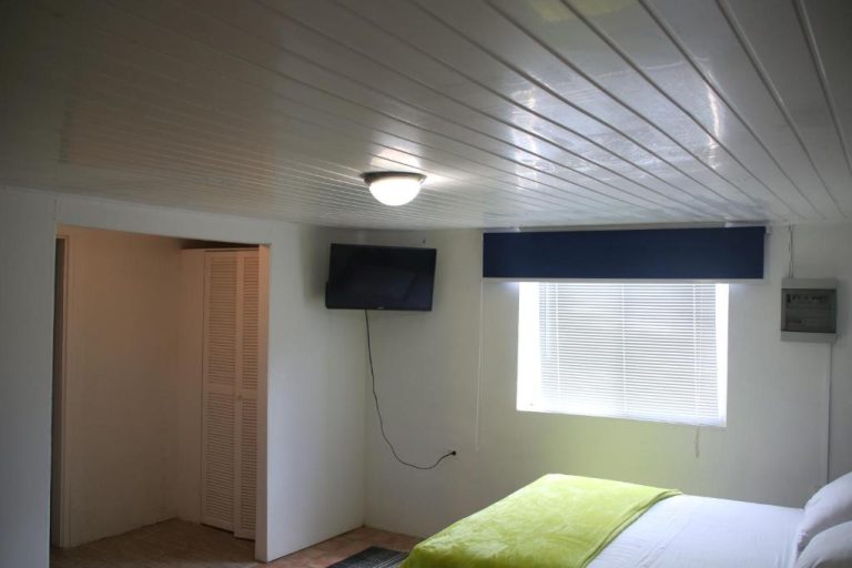 Habitación doble con televisión de pared y ventana con persiana azul en Coral Reef Beach
