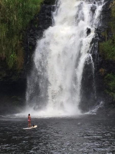 Mujer practicando paddle surf frente a la impresionante cascada del Inn at Kulaniapia Falls en Hawaii