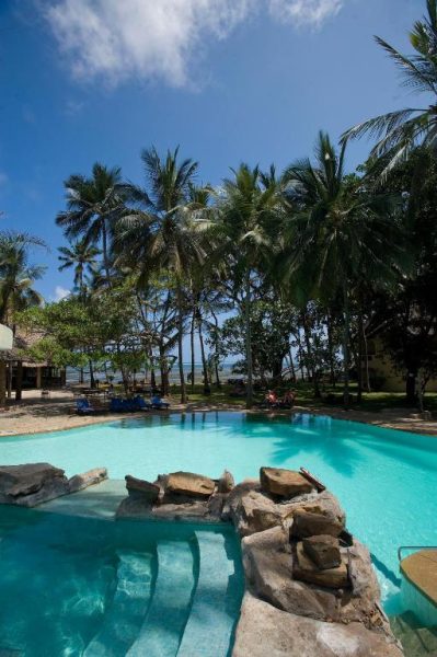 Piscina exterior con rocas naturales y palmeras tropicales en Severin Sea Lodge frente al océano