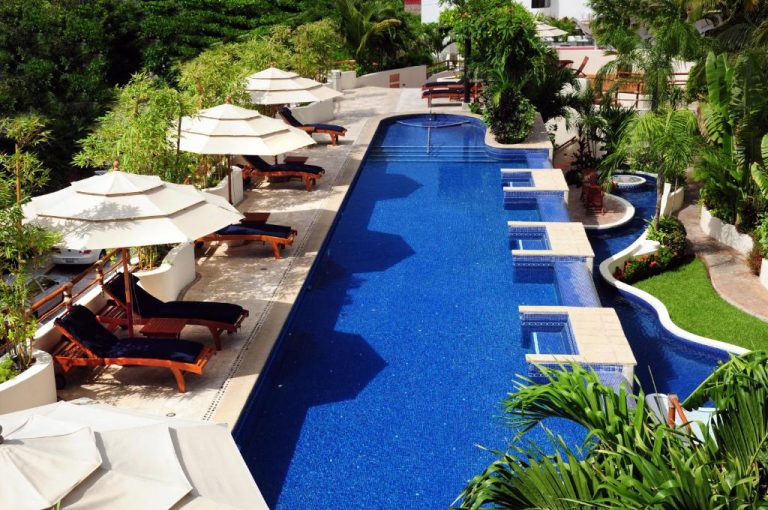 Piscina infinity con tumbonas y sombrillas del Porto Playa Condo Hotel and Beach Club rodeada de vegetación tropical