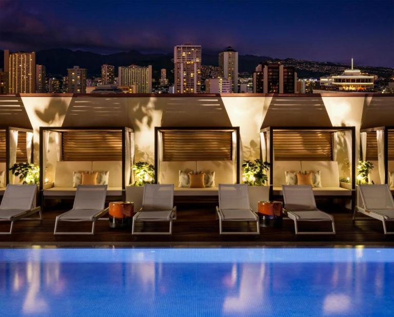 Piscina rooftop con cabañas de lujo y vistas nocturnas de la ciudad en Halepuna Waikiki by Halekulani