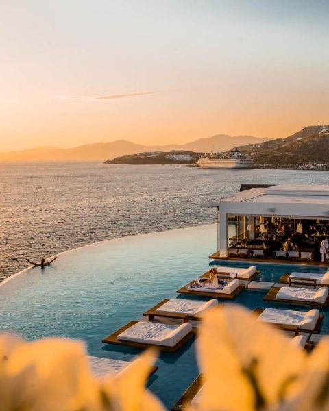 Piscina infinita con tumbonas flotantes y vistas al mar al atardecer en Cavo Tagoo Mykonos