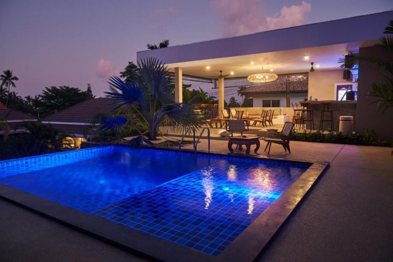 Piscina iluminada al atardecer con zona lounge y bar en Baan Sawan Samui Resort