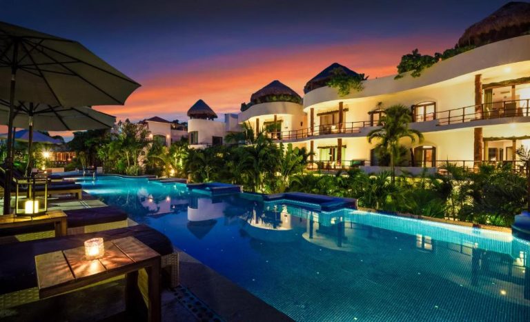 Piscina iluminada al atardecer del Porto Playa Condo Hotel and Beach Club con jardines tropicales